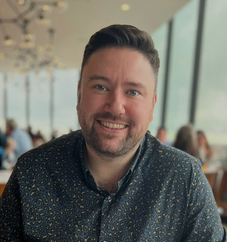 Professional headshot of Simon Deans in business attire smiling confidently